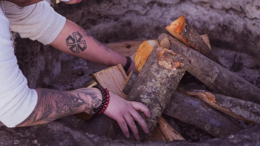 a man holding a knife next to a pile of wood, a tattoo, inspired by Elsa Bleda, pexels contest winner, land art, fire pit, video still, background image