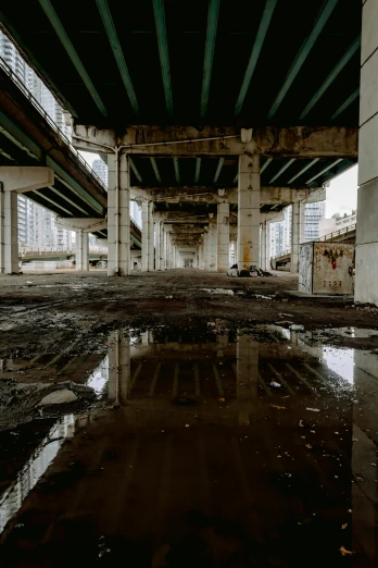 a large puddle of water under a bridge, an album cover, inspired by Thomas Struth, unsplash contest winner, post apocalyptic city, intersection, urbex, high rises