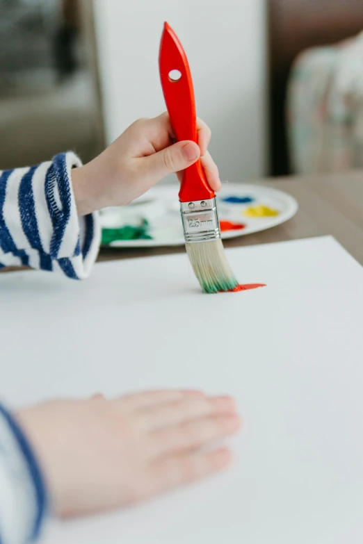 a child is painting on a piece of paper, pexels contest winner, on a white table, long paint brush strokes, primary colors are white, textured canvas