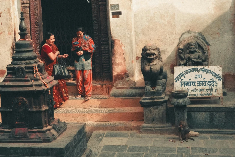a couple of women standing in front of a building, a statue, by Daniel Lieske, pexels contest winner, bengal school of art, in an ancient altar, in a village street, 🦩🪐🐞👩🏻🦳, trampling an ancient city