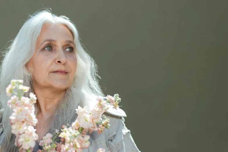 a woman holding a bunch of flowers in her hands, an album cover, inspired by Annie Leibovitz, trending on unsplash, photorealism, light gray long hair, elderly greek goddess, dayanita singh, facing sideways