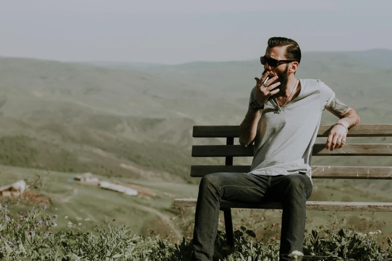 a man sitting on top of a wooden bench, pexels contest winner, drinking and smoking, on a hill, avatar image, unshaven