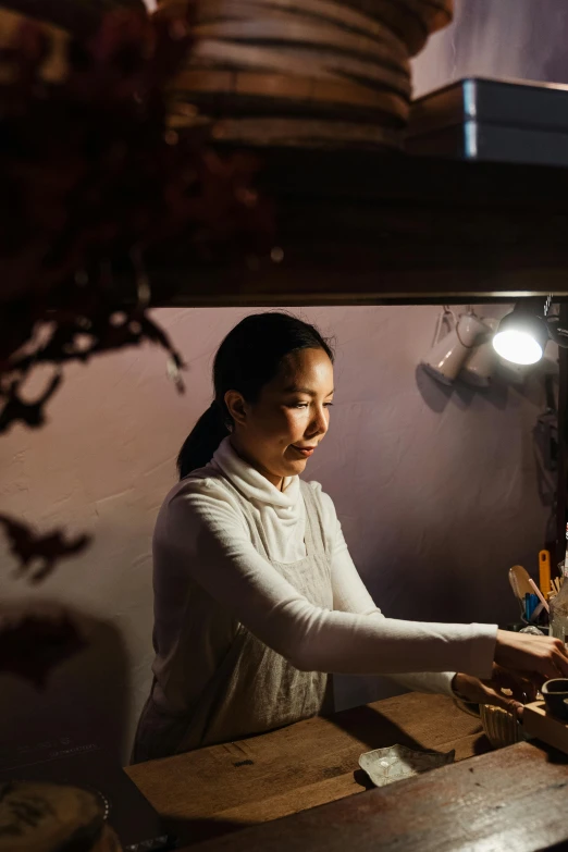 a woman standing at a counter in a kitchen, a portrait, inspired by Cui Bai, pexels contest winner, ambient cave lighting, working in the forge, tea ceremony scene, under studio lighting