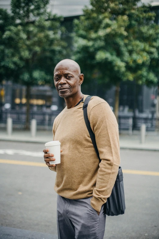 a man standing on the side of the road holding a cup of coffee, by Christopher Williams, trending on unsplash, renaissance, portrait of samuel l. jackson, mature male, people walking around, 15081959 21121991 01012000 4k