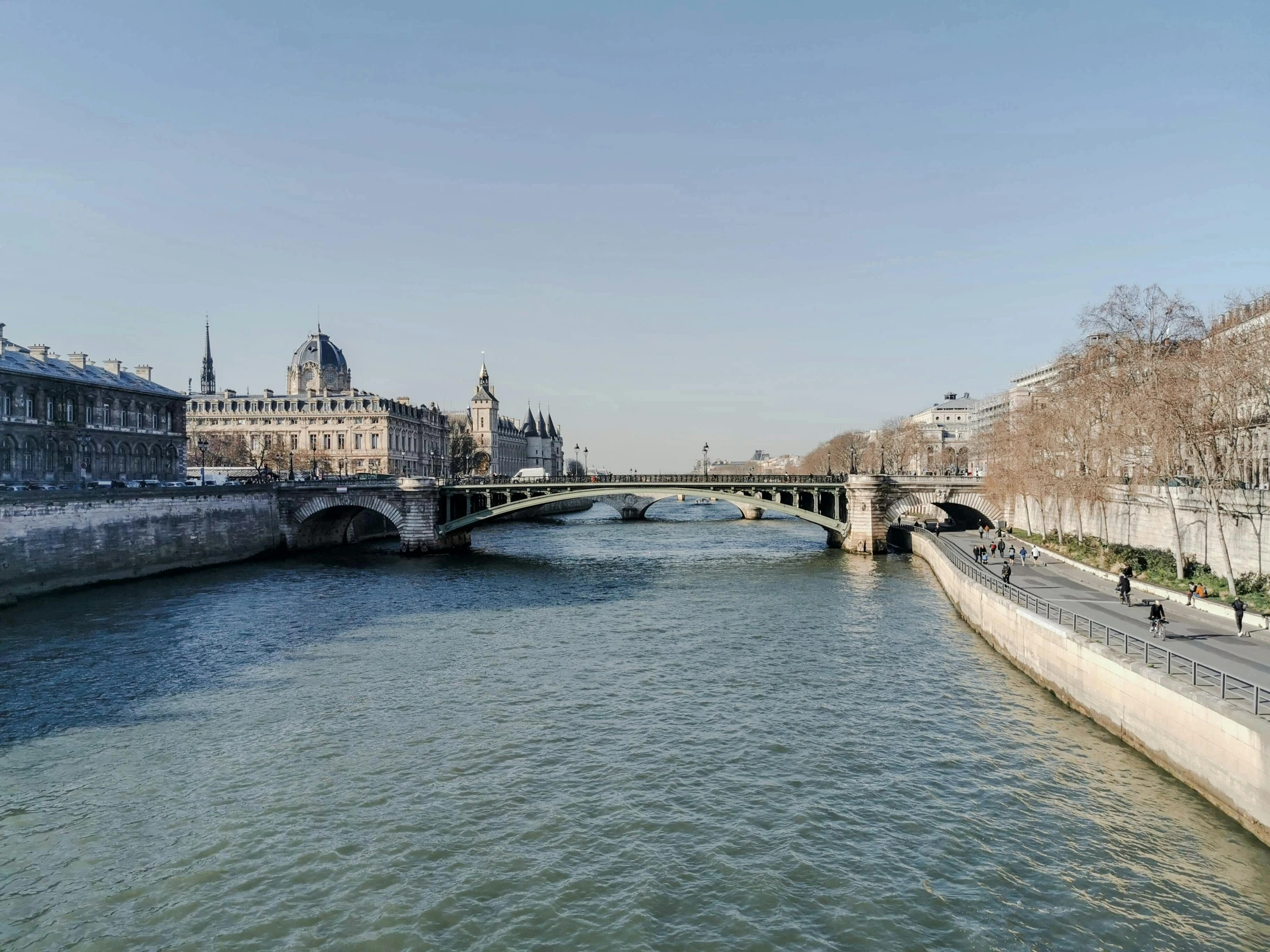 a river running through a city next to tall buildings, musée d'orsay catalogue, bridge over the water, sunny day time, grey