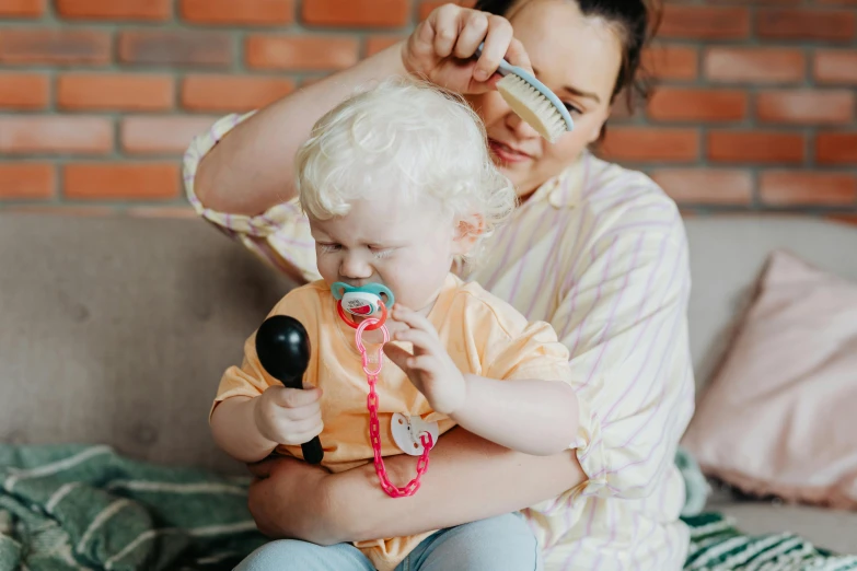 a woman combing a child's hair while sitting on a couch, pexels contest winner, holding a bell, third trimester, with a stethoscope, lachlan bailey