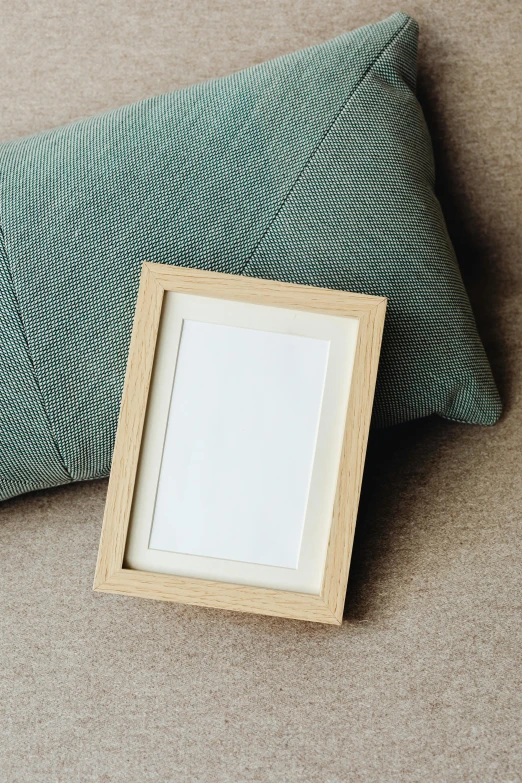 a picture frame sitting on top of a pillow next to a pillow, unsplash, oak, square shapes, soft colore, small