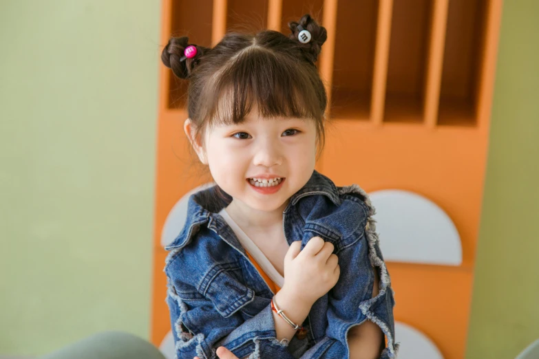 a little girl sitting on top of a chair, inspired by Mei Qing, pexels contest winner, wearing a jeans jackets, twintails hairstyle, cute smiling face, medium close-up shot