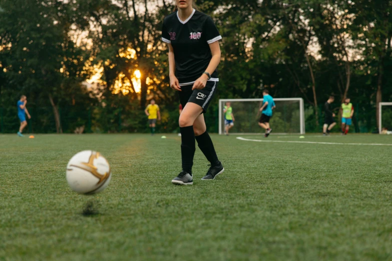 a woman kicking a soccer ball on a field, pexels contest winner, wearing black shorts, 15081959 21121991 01012000 4k, evening time, university