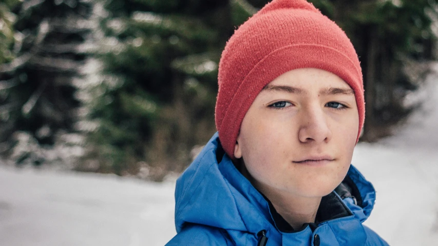 a close up of a person wearing a red hat, by Emma Andijewska, teenage boy, only snow in the background, proud serious expression, avatar image