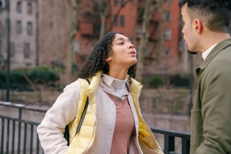 a man and a woman standing next to each other, trending on pexels, happening, arguing, young woman looking up, wearing a yellow hoodie, curly haired