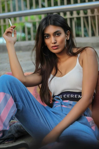 a woman sitting on the ground smoking a cigarette, trending on cg society, red tank top and wide blue pants, indian super model, tanned ameera al taweel, wearing white camisole
