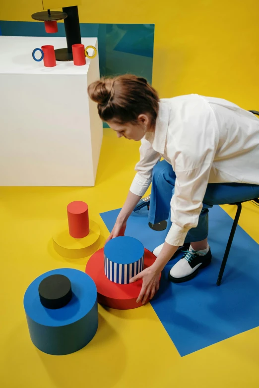 a woman sitting on top of a blue chair, inspired by Bauhaus, trending on unsplash, de stijl, art toys on a pedestal, stepping on towers, dezeen showroom, high angle