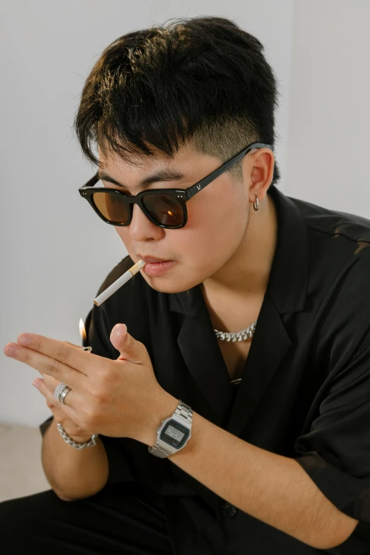 a man sitting on the ground smoking a cigarette, an album cover, inspired by Xia Yong, trending on pexels, wearing square glasses, androgynous, profile image, with index finger