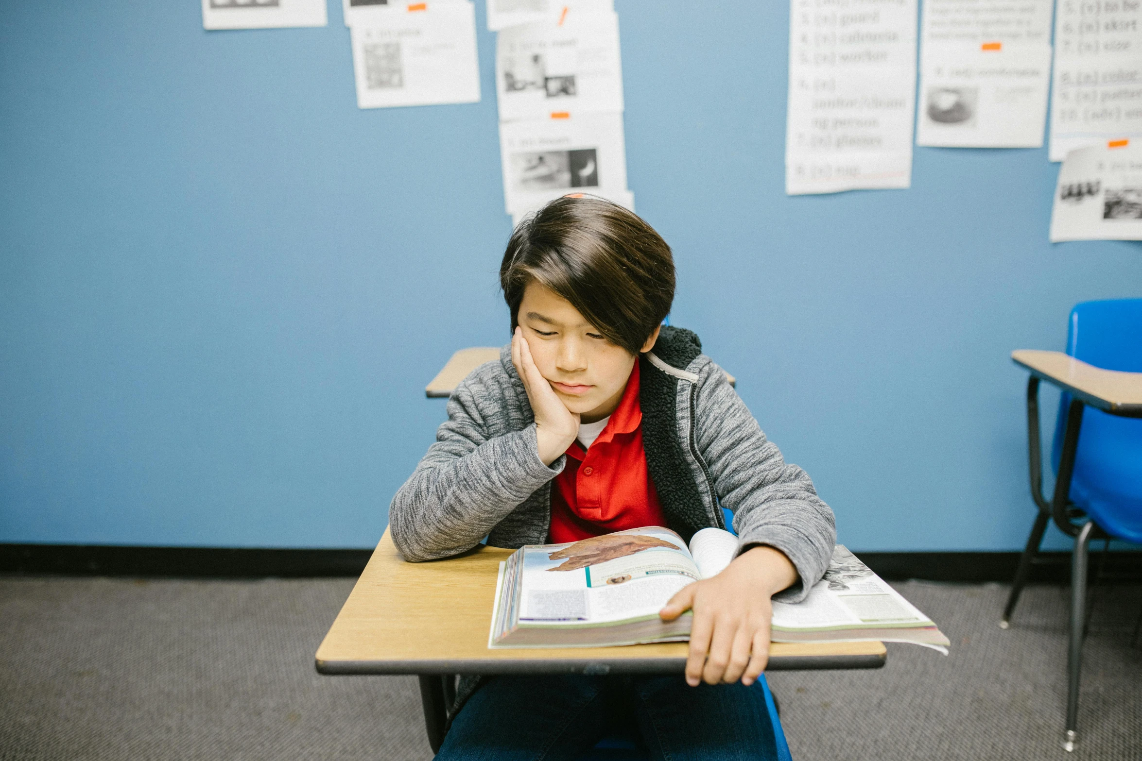 a young boy sitting at a desk reading a book, trending on unsplash, vancouver school, looking tired, in a classroom, damien tran, aged 13