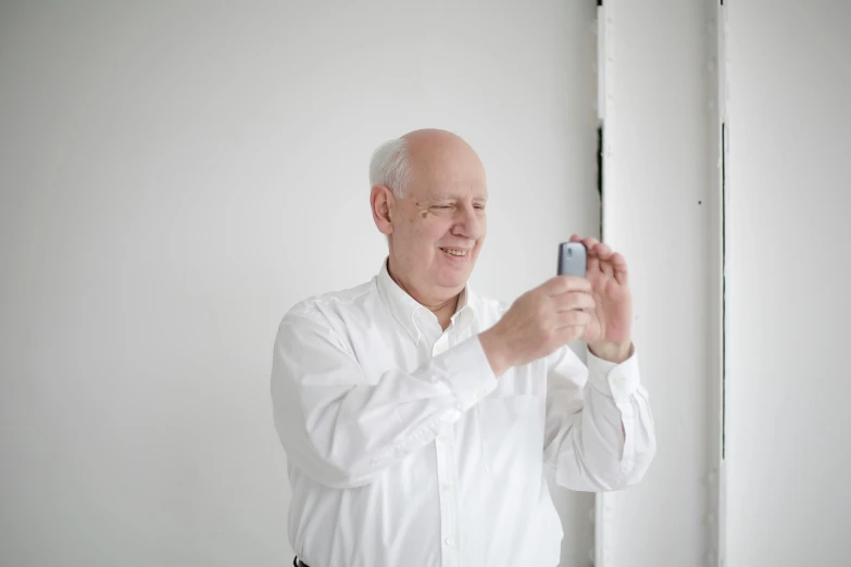 a man taking a picture of himself in a mirror, inspired by Richard Wilson, unsplash, photorealism, in front of white back drop, holding a very advance phone, hide the pain harold, while smiling for a photograph