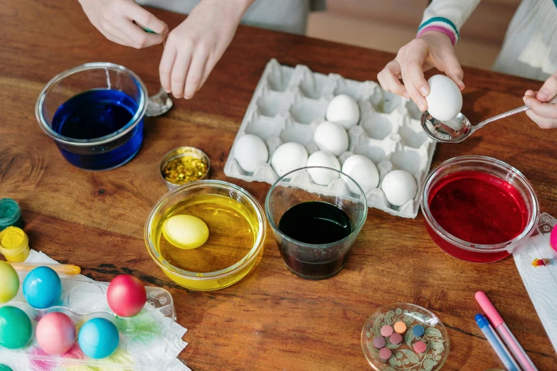 a group of people painting eggs on a table, on a wooden desk, beakers of colored liquid, 🦩🪐🐞👩🏻🦳, recipe