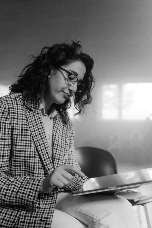 a black and white photo of a woman reading a book, by Niyazi Selimoglu, wearing a suit and glasses, screenwriter, on a desk, ameera al-taweel