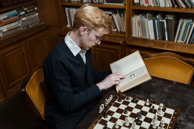 a man sitting at a table playing a game of chess, inspired by Simon Marmion, pexels contest winner, academic art, with one vintage book on a table, library nerd glasses, looks like domhnall gleeson, 15081959 21121991 01012000 4k