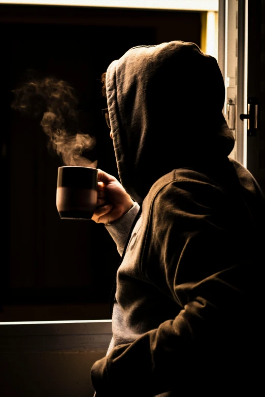 a person in a hoodie holding a cup of coffee, by Eglon van der Neer, pexels contest winner, dramatic backlit window, smoker, a cozy, scary