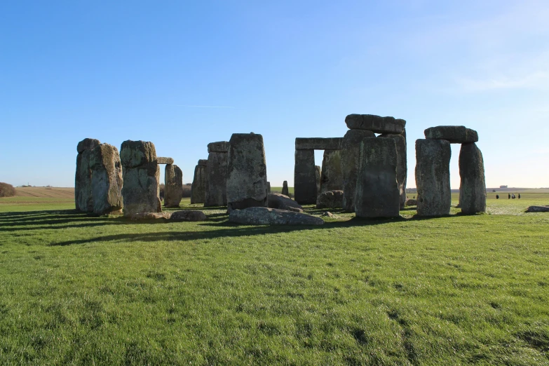 a group of stonehenks standing on top of a lush green field, a marble sculpture, stonehenge, flagstones, buildings, blue sky