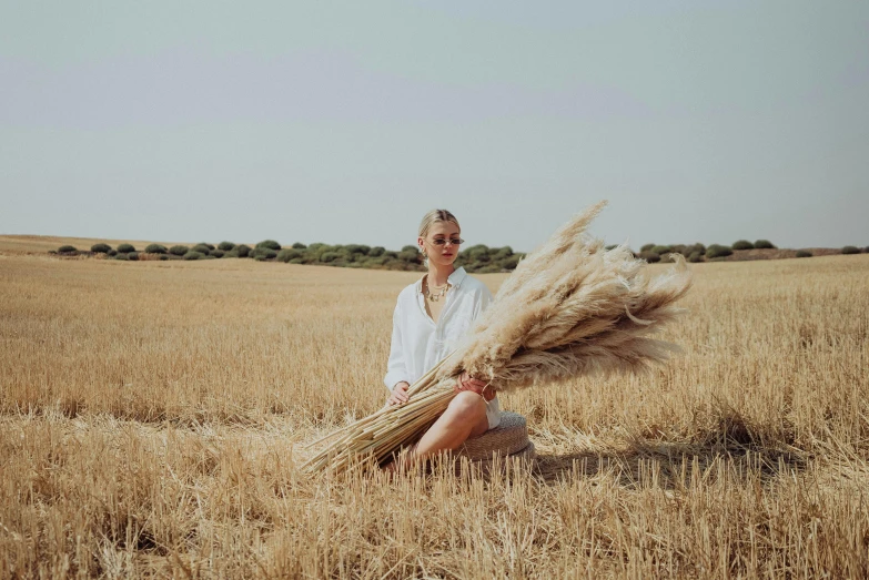 a woman sitting in a field holding a bunch of wheat, by Emma Andijewska, land art, blonde, agrigento, slightly minimal, instagram photo