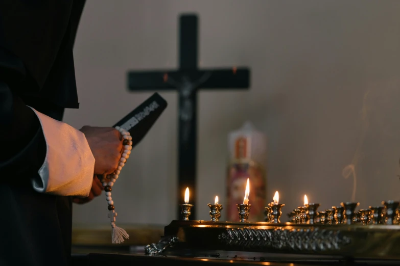 a person holding a cell phone in front of a bunch of candles, religious robes, on a candle holder, shadow of the cross, profile image