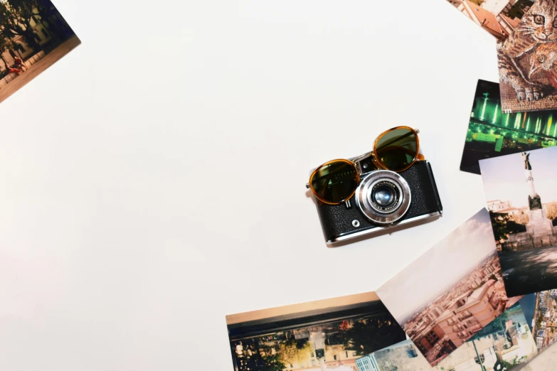 a camera sitting on top of a table next to pictures, by Gavin Hamilton, trending on pexels, designer sunglasses, on a white background, conde nast traveler photo, mixed art