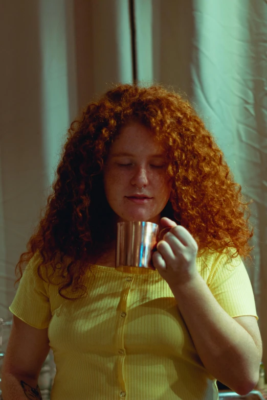 a woman with red hair drinking from a cup, an album cover, inspired by Nan Goldin, pexels, renaissance, movie still frame, curly copper colored hair, is ((drinking a cup of tea)), high resolution film still