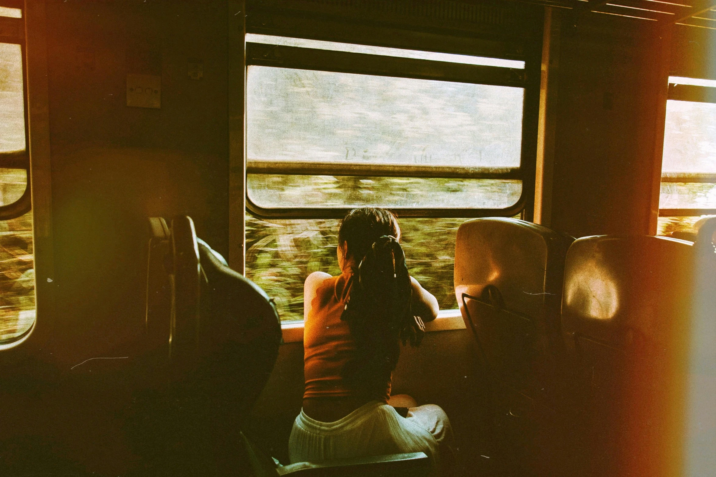 a woman sitting on a train looking out the window, by Lucia Peka, pexels contest winner, redscale photography, on a yellow canva, her back is to us, 🚿🗝📝