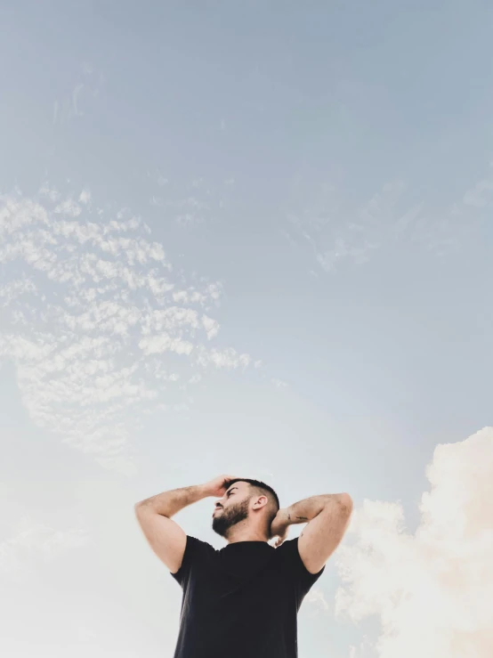 a man standing on top of a sandy beach, trending on unsplash, aestheticism, men look up at the sky, wearing a black tshirt, in front of white back drop, on clouds