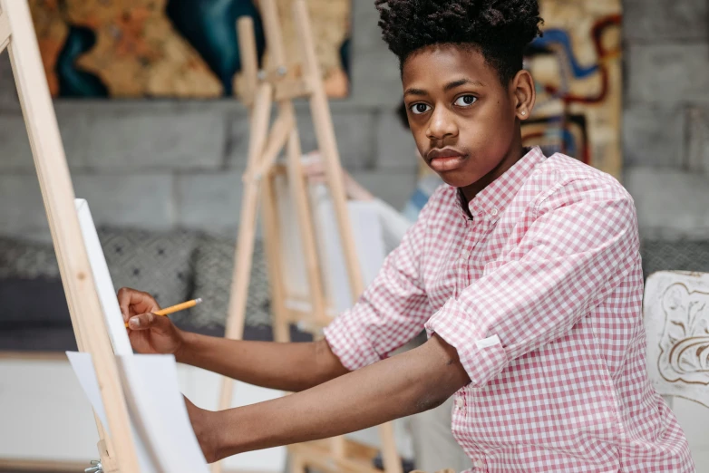 a young boy is painting on an easel, a hyperrealistic painting, trending on pexels, academic art, black teenage boy, androgynous person, looking serious, thumbnail