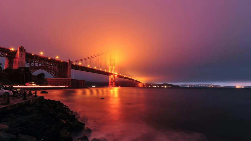 the golden gate bridge is lit up at night, pexels contest winner, romanticism, light orange mist, maroon mist, hyper color photograph, grain”