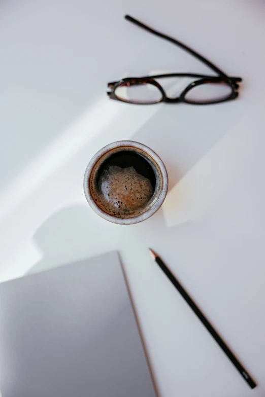 a cup of coffee sitting on top of a white table, by Robbie Trevino, trending on pexels, process art, round black glasses, medium: black pencil, pictured from the shoulders up, product introduction photo