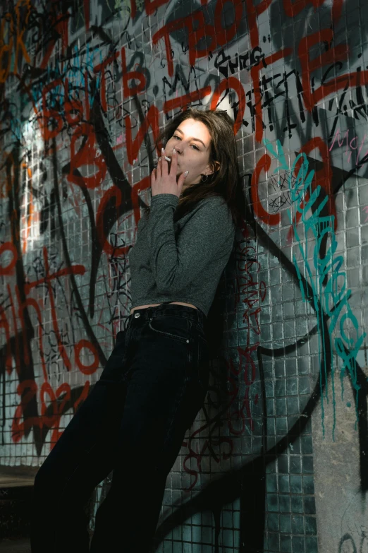 a woman leaning against a wall covered in graffiti, an album cover, inspired by Elsa Bleda, pexels contest winner, hailee steinfeld, smoking and bickering, gray skin. grunge, infp young woman