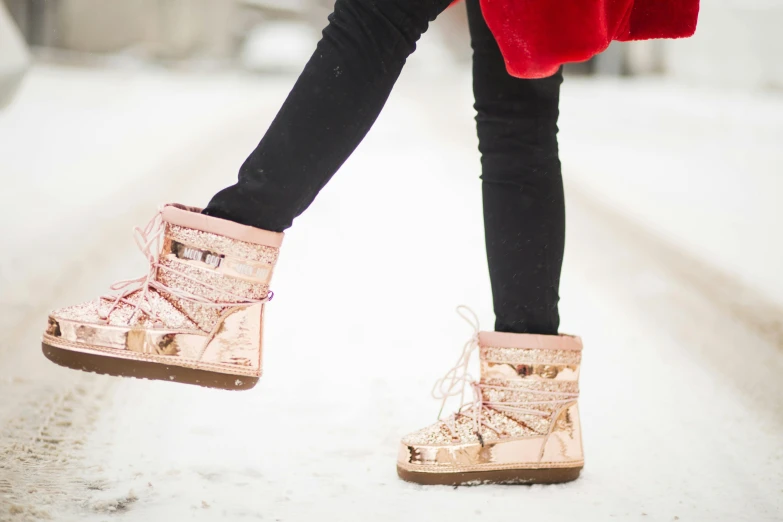 a woman in a red coat is walking in the snow, a photo, trending on pexels, pink and gold, wearing boots, standing in gold foil, girls