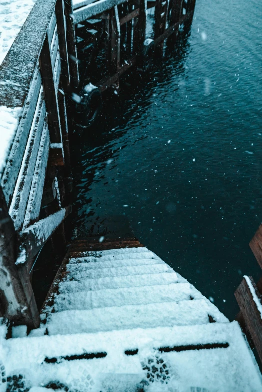 a pier covered in snow next to a body of water, an album cover, inspired by Elsa Bleda, pexels contest winner, happening, coming down the stairs, high angle close up shot, subsurface scandering, cold colors