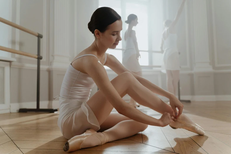 a woman sitting on the floor tying up her ballet shoes, by Elizabeth Polunin, pexels contest winner, arabesque, in white room, pretty face with arms and legs, sydney hanson, anna nikonova aka newmilky
