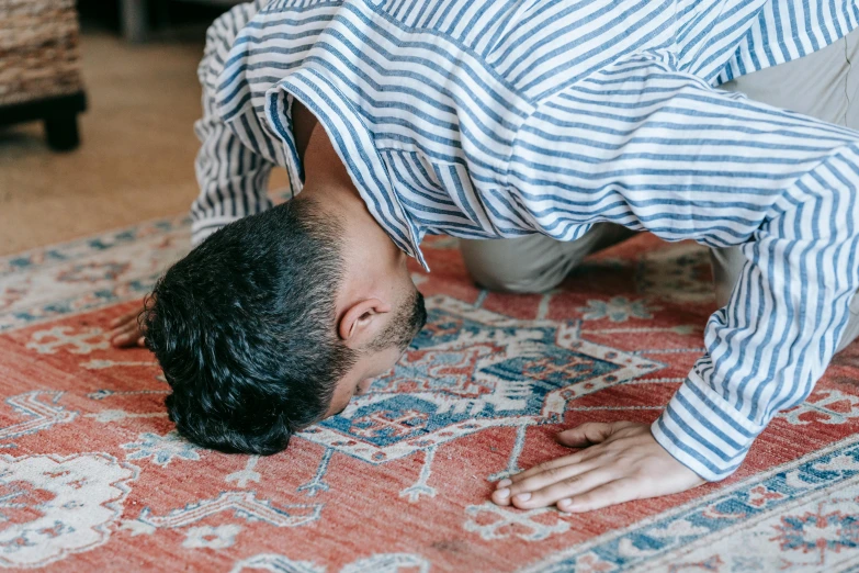 a man is doing a handstand on a rug, by Carey Morris, hurufiyya, kneeling in prayer, indoor picture, background image, medium-shot