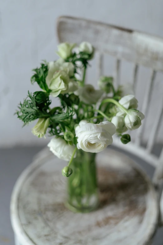 a green vase filled with white flowers sitting on a chair, inspired by Alfred Jensen, romanticism, anemone, with a long white, medium close up, tufted softly