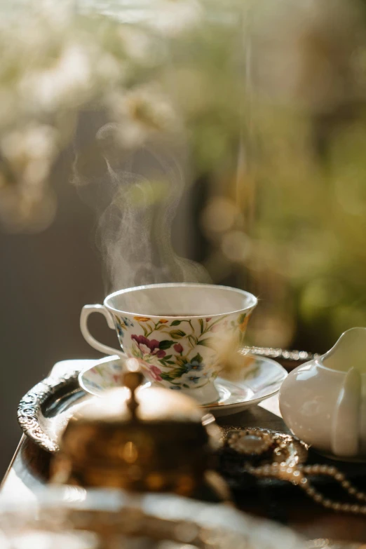 a tea pot sitting on top of a table next to a cup, by Jessie Algie, trending on pexels, rococo, gentle smoke effect, golden light, profile image, lush surroundings