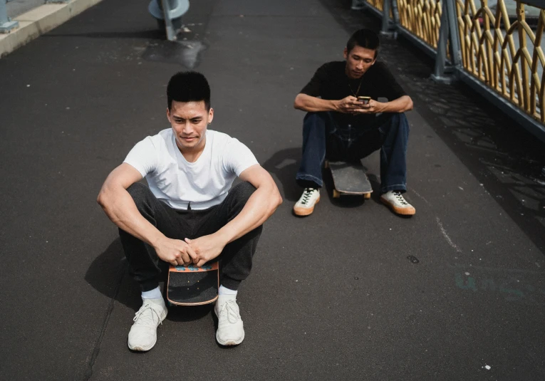 a man sitting on a skateboard next to another man, david luong, looking to camera, kuntilanak, high quality photo