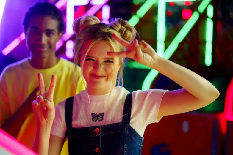 a woman making a peace sign while standing next to a man, neon lights in the background, samara weaving, softplay, a busy arcade