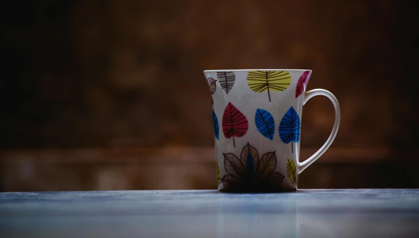 a close up of a coffee cup on a table, by Jessie Algie, pexels contest winner, process art, colorful leaves, mug shot, retro colour, plain background