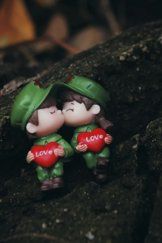 a couple of figurines sitting on top of a rock, by Valentine Hugo, pexels contest winner, vietnam war, love theme, elves, kissing