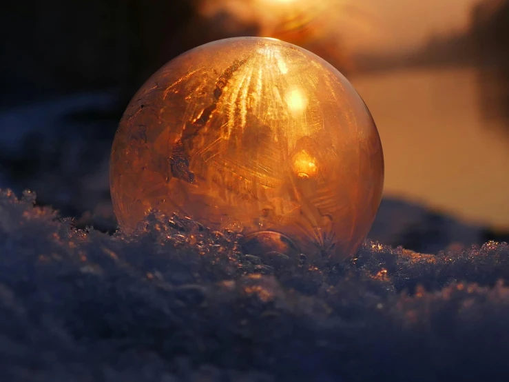 a glass ball sitting on top of snow covered ground, during a sunset