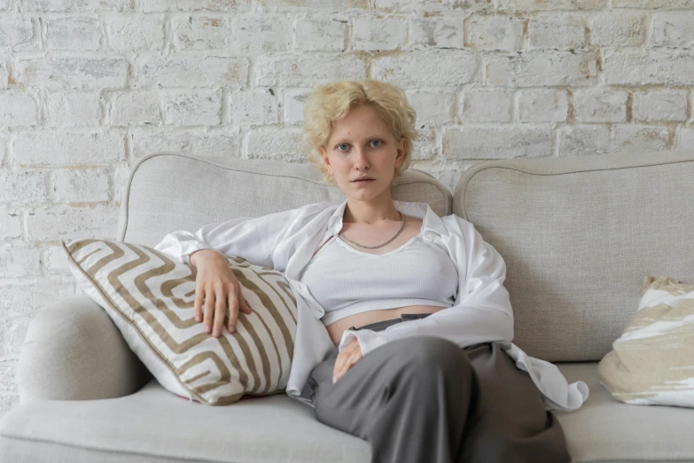 a woman sitting on a couch with a pillow, inspired by Anna Füssli, pexels, pale skin curly blond hair, angry look, white russian clothes, belly button showing