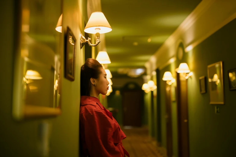 a woman in a red shirt standing in a hallway, inspired by Wes Anderson, unsplash, hotel room, green lights, yellow lighting from right, gemma chen