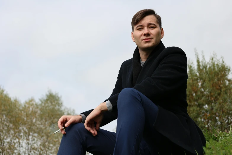 a man sitting on top of a lush green hillside, an album cover, by Adam Marczyński, pexels contest winner, magic realism, he is wearing a black trenchcoat, sitting on a park bench, julian ope, portrait of ernest khalimov