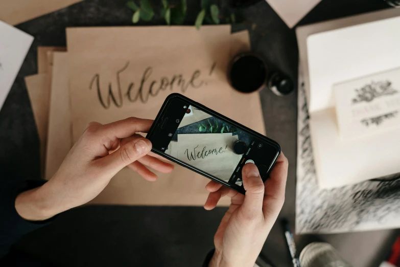 a person taking a picture of a welcome sign on a cell phone, trending on pexels, estrange calligraphy, thumbnail, background image, handcrafted